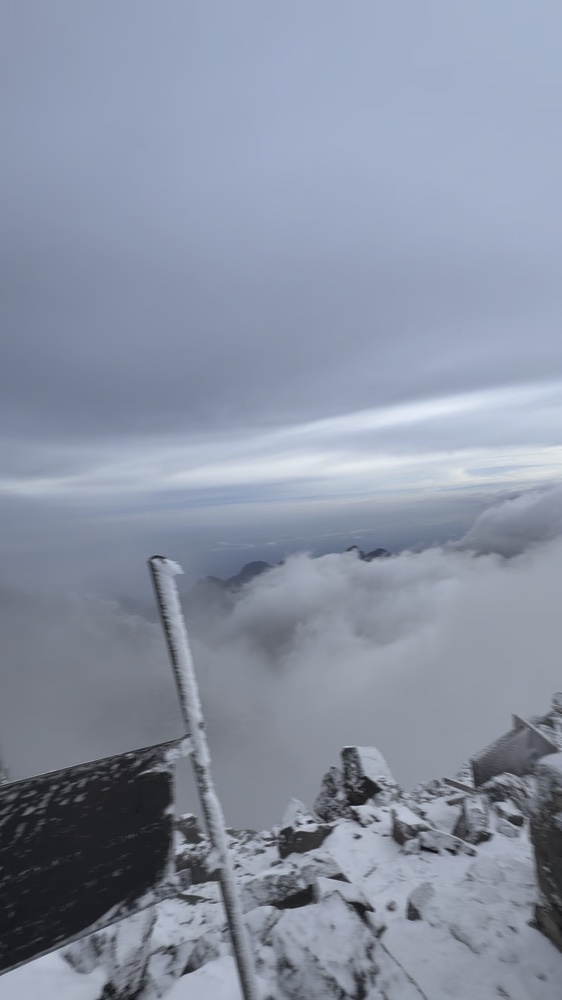 Snow-covered summit rocks above layers of cloud